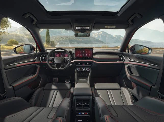 Premium all-black interior cabin of Skoda Kodiaq RS featuring a 13-inch touchscreen, sporty steering wheel, red ambient lighting, and a panoramic sunroof.